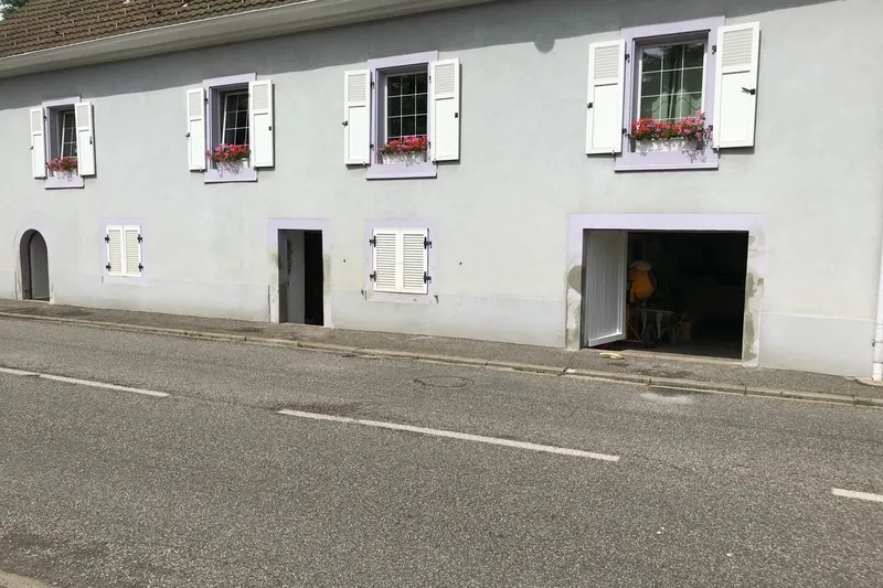 Façade de maison de village repeinte, volets blancs et fenêtres fleuries