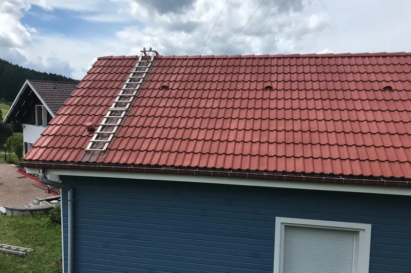 Toiture en tuiles rouges rénovée sur une maison en bardage bois bleu