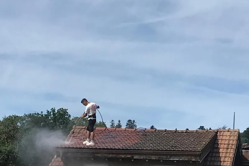 Rinçage d'une toiture en tuiles depuis le toit, nuage d'eau au-dessus de la maison